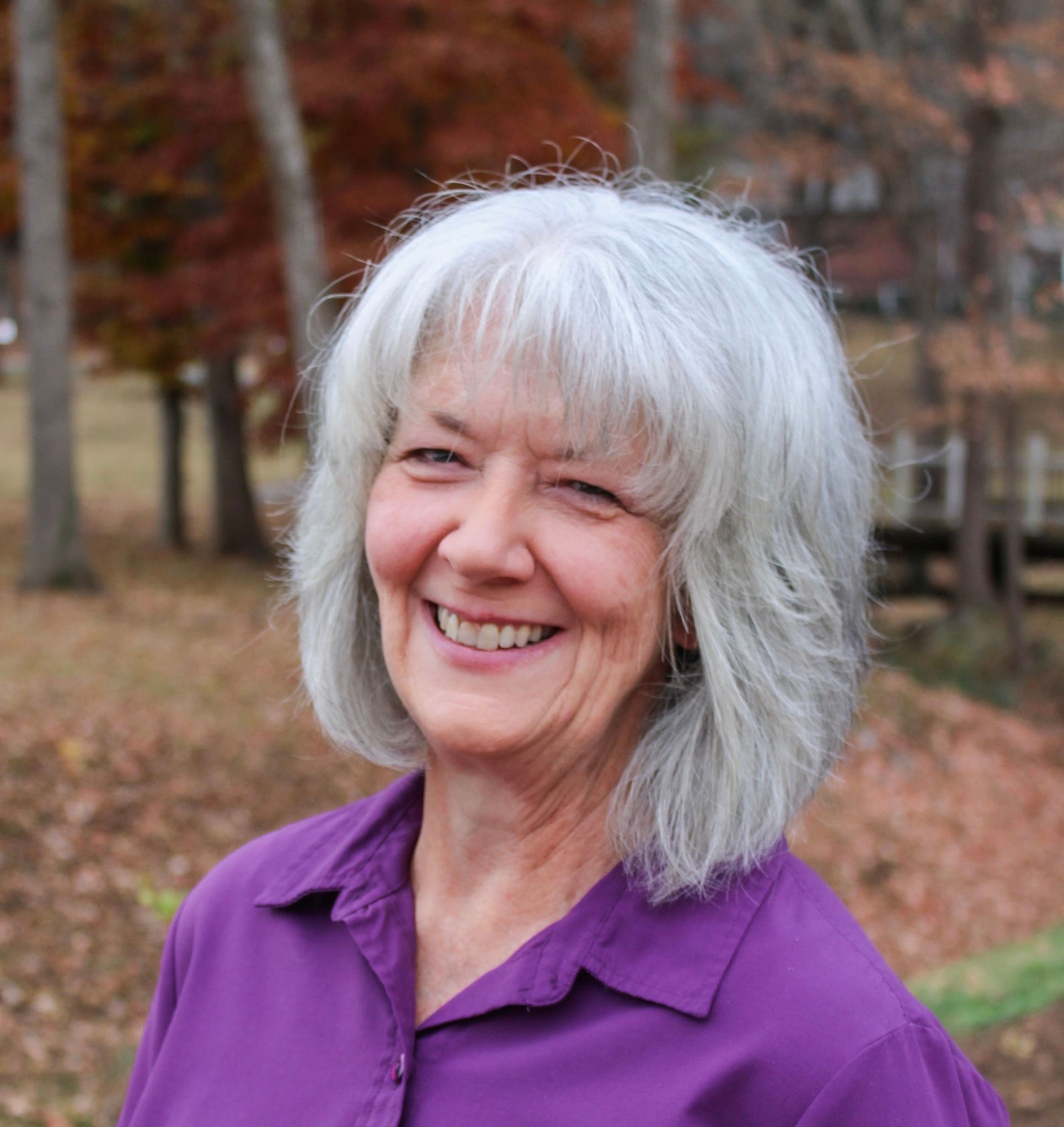 Karen Taylor smiling outdoors among autumn trees